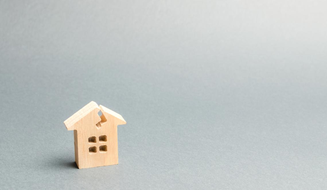 A wooden house with a crack. The concept of a damaged house, dilapidated housing. Home repair after disaster. Renovation, restoration of the old building. Property insurance. Damage. Weather element.