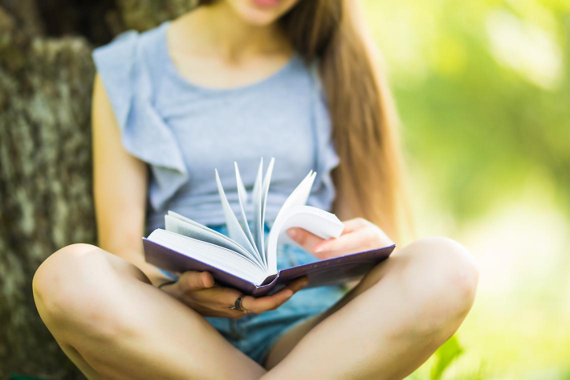 Pretty girl reading book in the park. Student preparing for the exam. Literary leisure outdoor.