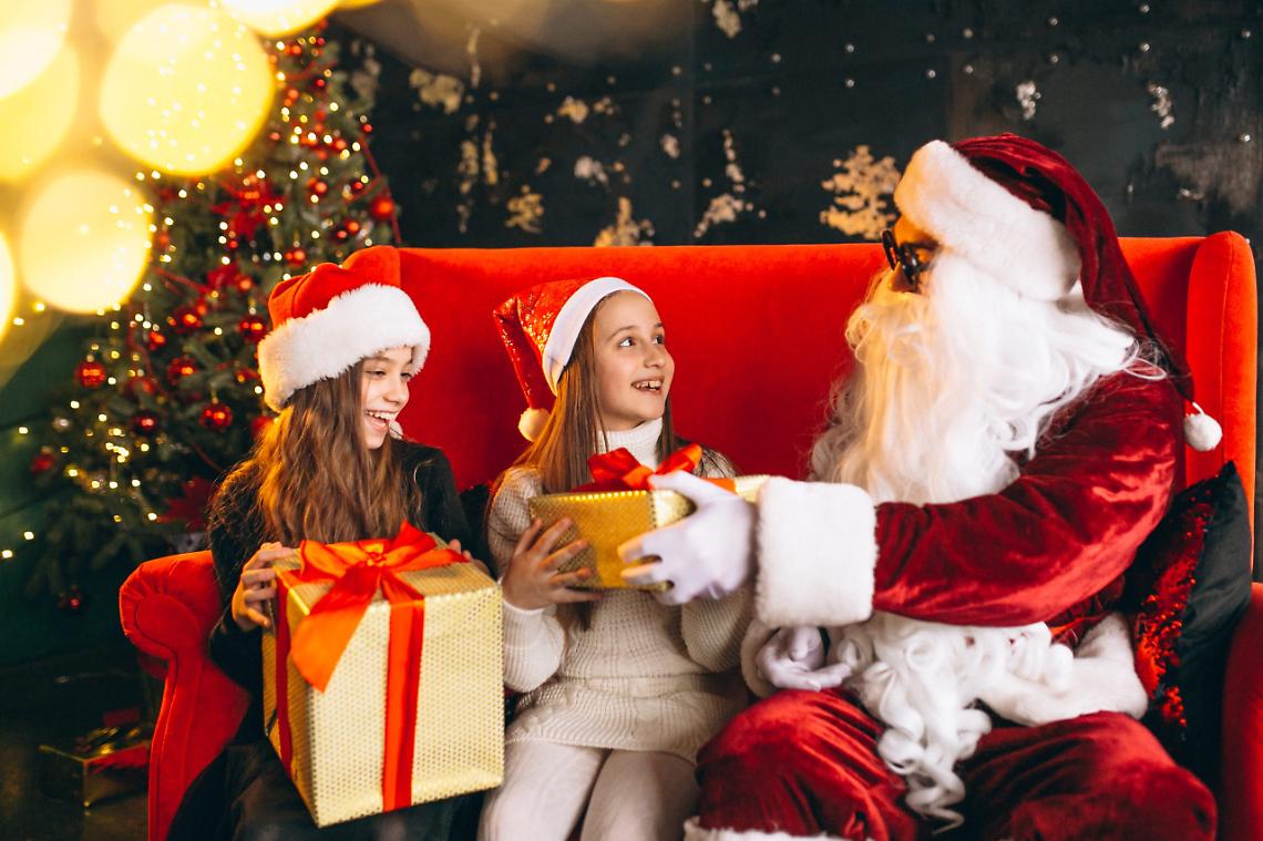 Group of kids sitting with santa and presents on christmas eve