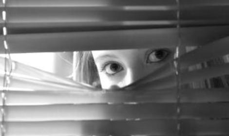 Young female looking through window blinds at night.(shallow depth of field)