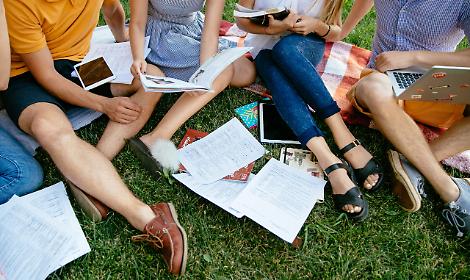 Group of students with books and tablet are studying outdoors together